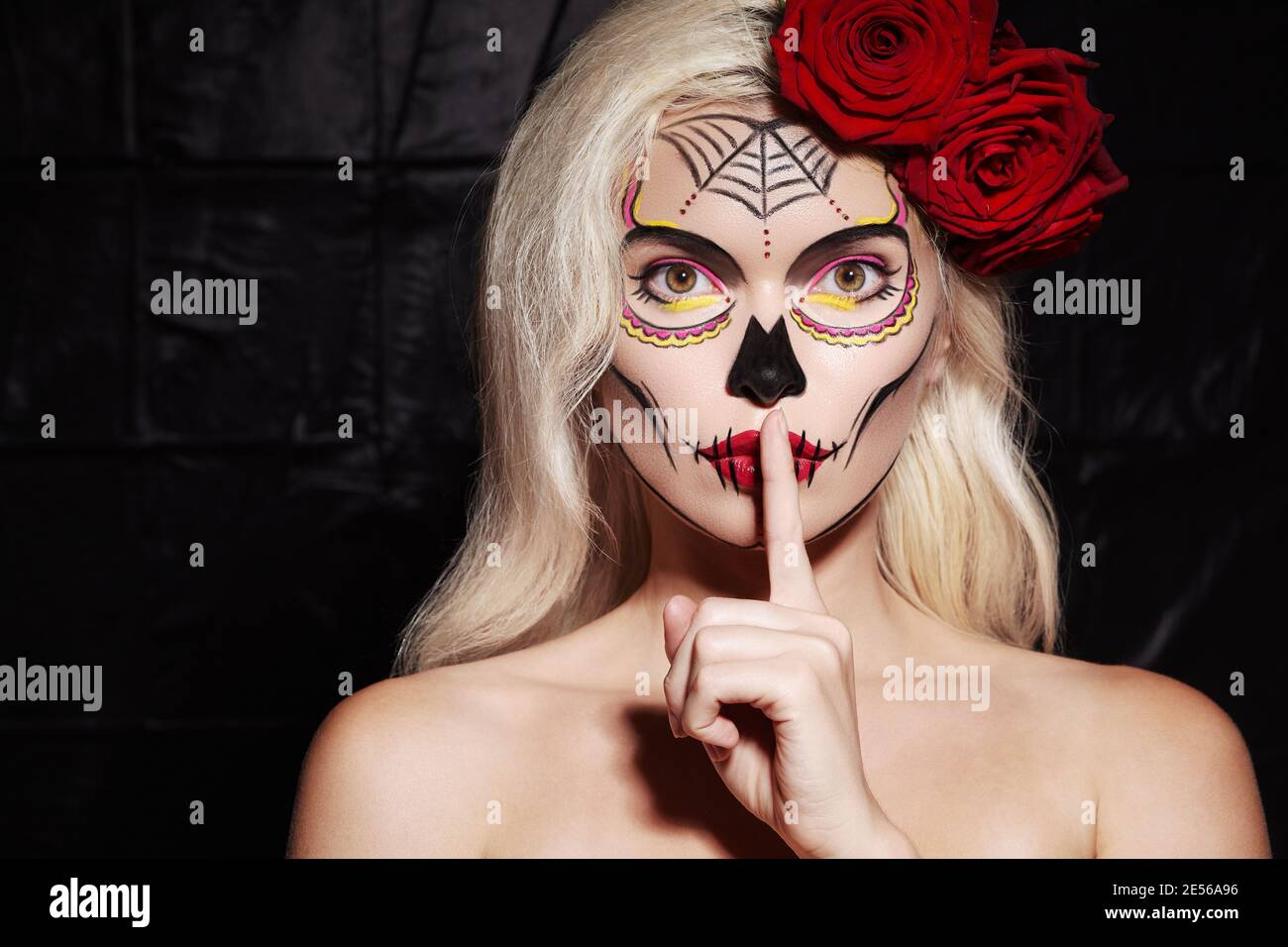 Beautiful Halloween Make-Up Style. Blond Model Wear Sugar Skull Makeup with Red Roses, pale Skin Tones and Waves Hair. Santa Muerte concept. Silence G Stock Photo