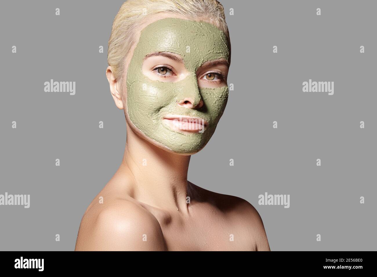 Beautiful Woman Applying Green Facial Mask. Beauty Treatments. Close-up Portrait of Spa Girl Apply Clay Facial mask on grey background. Stock Photo