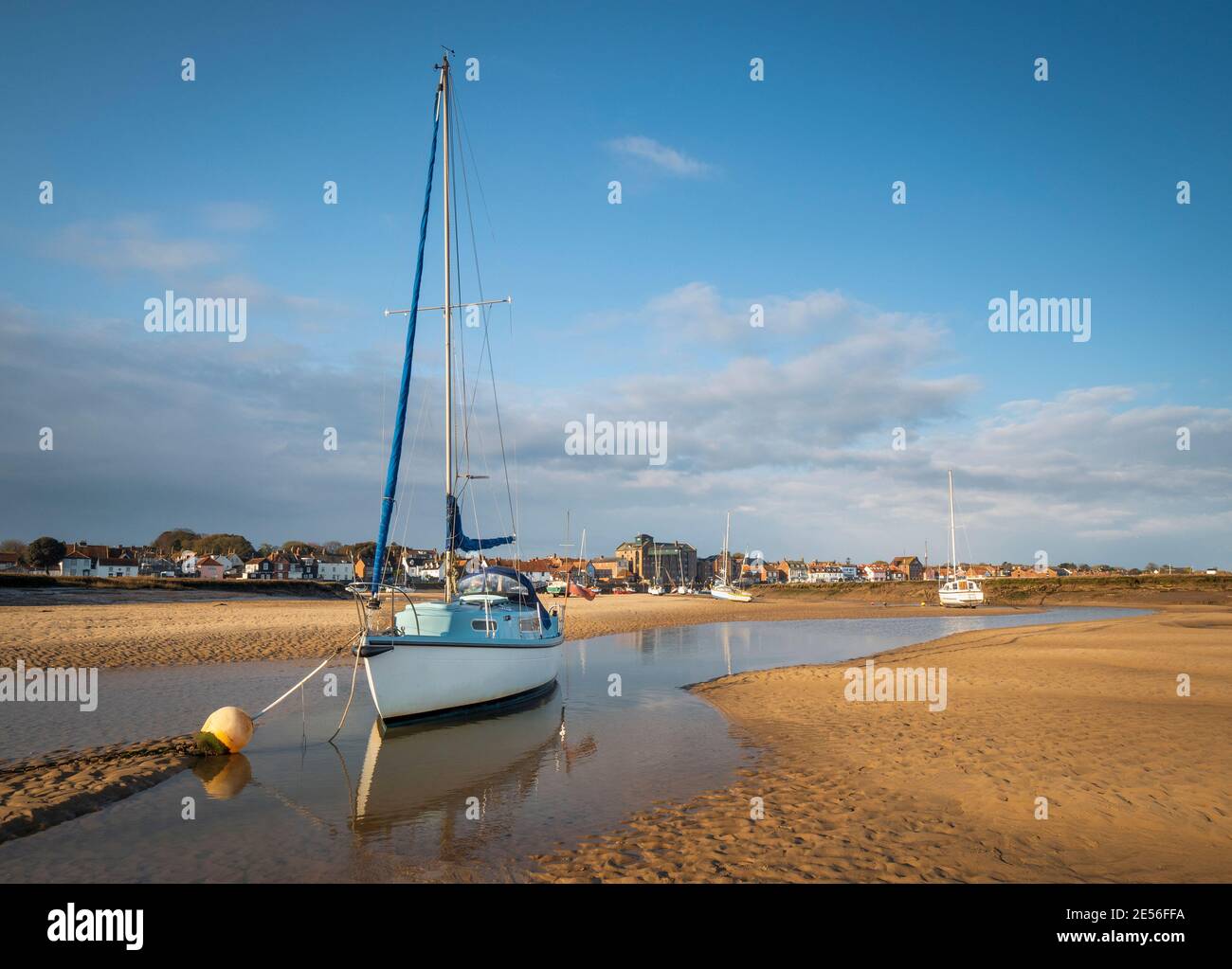 A blue and white sailing boat on the sand bank of Wells-Next-the-Sea at low tide. Stock Photo