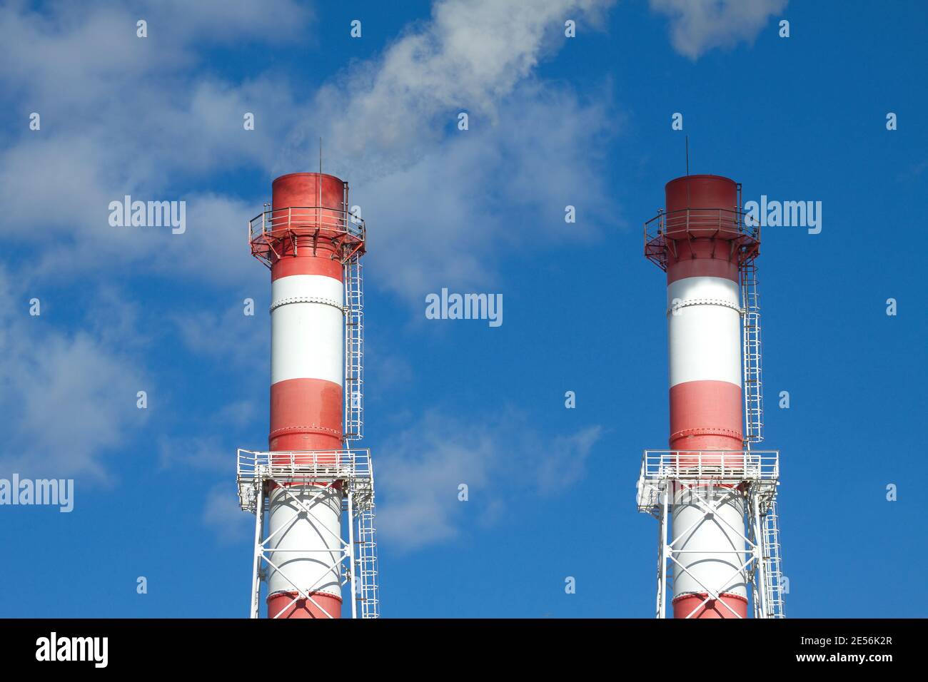 Top part of two big color industrial smoke pipes over blue sky with ...