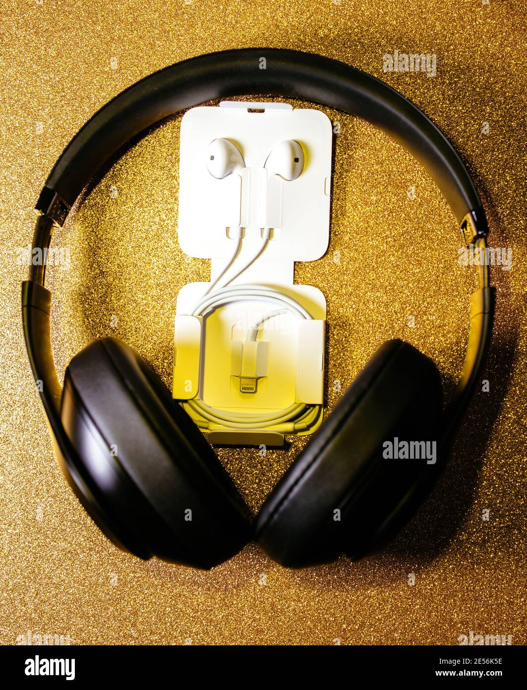 Paris, France - Oct 2, 2018: Apple Computers EarPods headphones with lightning connector on the golden sparkling background with large Beats By Dr Dre black headphones Stock Photo