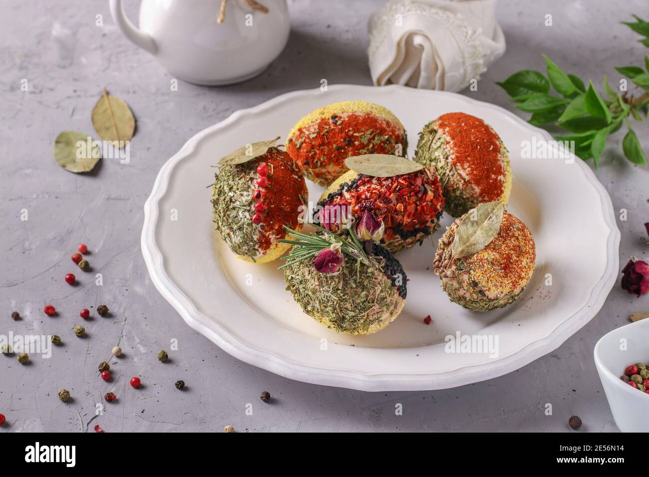 Easter eggs decorated with different spices and cereals without dyes and preservatives on a white plate on a gray concrete background. Stock Photo