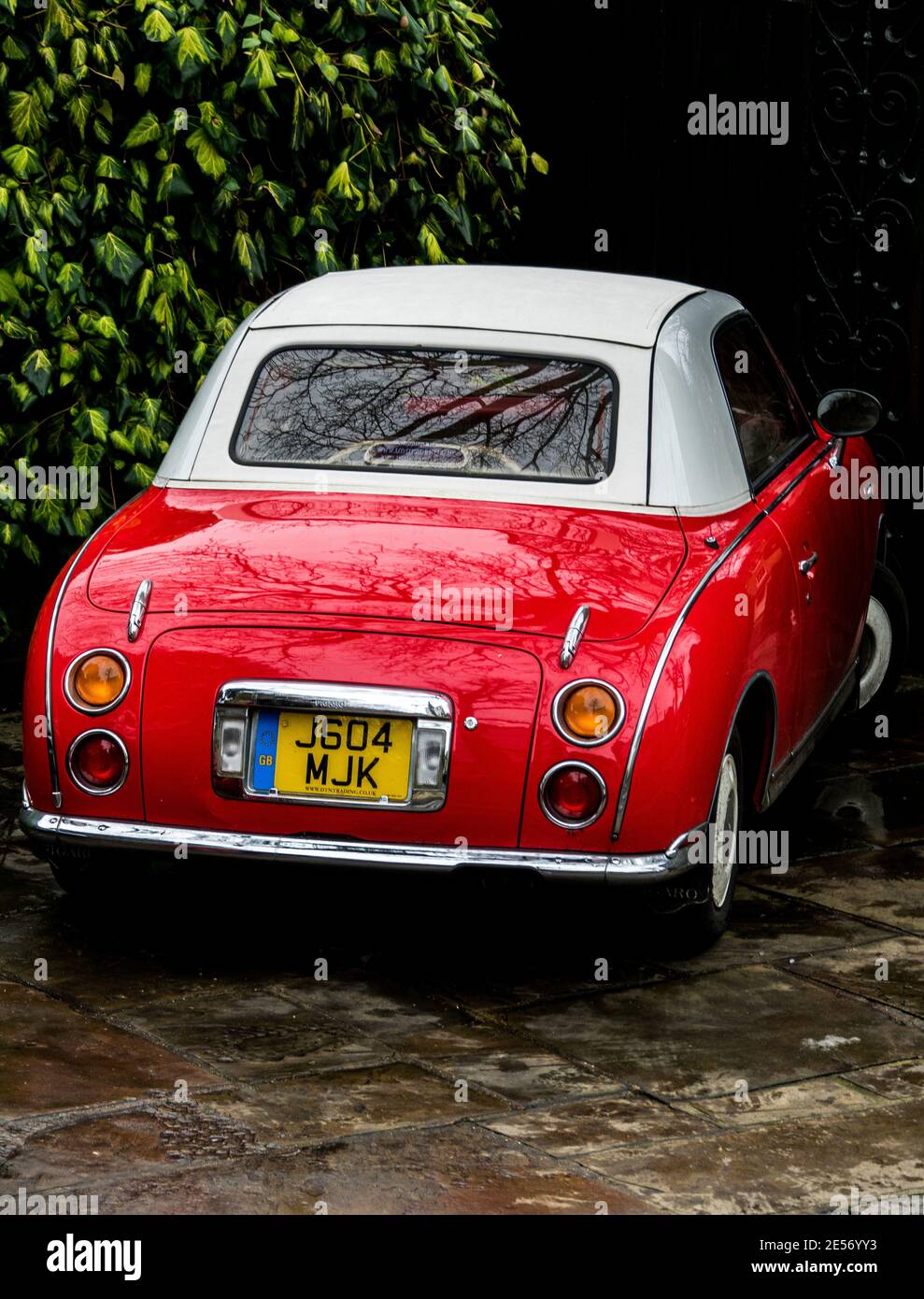 Red Nissan Figaro, a convertible car, parked at the side of the road