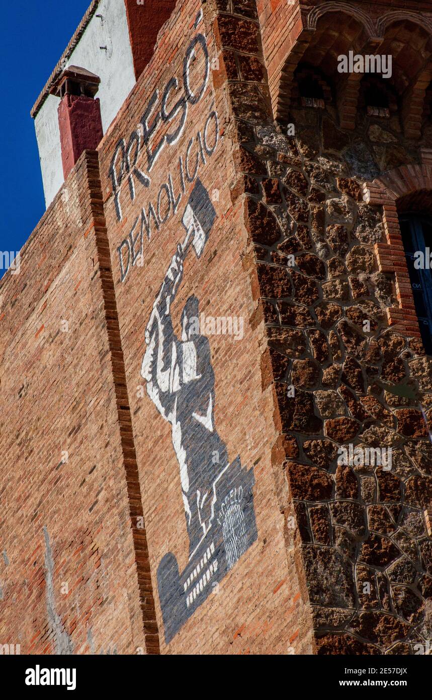 Large stencilled graffito high up on brick wall of building in central Barcelona depicting a man destroying a prison - wording reads Preso Demolicio Stock Photo