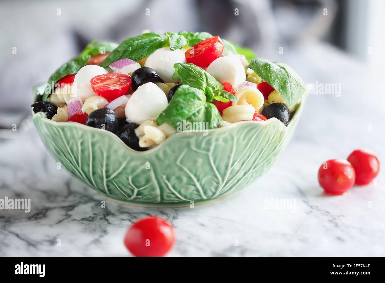 Italian pasta salad with fresh tomatoes, black olives, red onion mozzarella cheese balls, basil, and an olive oil dressing over marble table. Extreme Stock Photo
