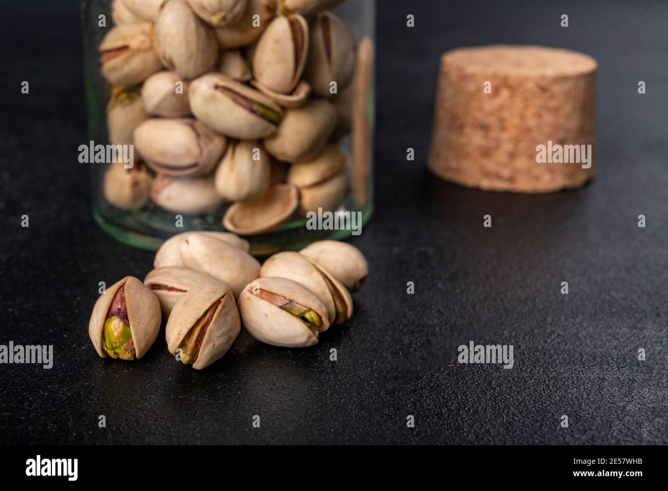 Pistachio nuts on a dark table. Salty snack in a jar. Dark background. Stock Photo