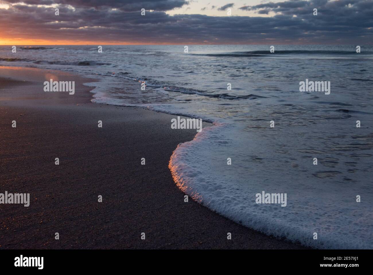 Sunlight glimmers on seafoam and the water's edge as a new day begins at Atlantic Beach, North Carolina. Stock Photo