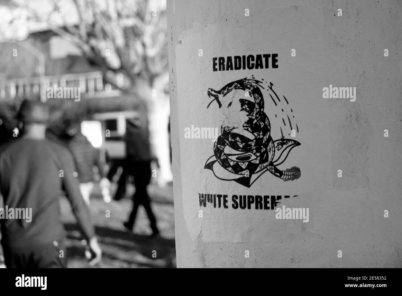 'Eradicate White Supremacy' flyer seen at Lake Merritt with the back of black man walking away. Stock Photo