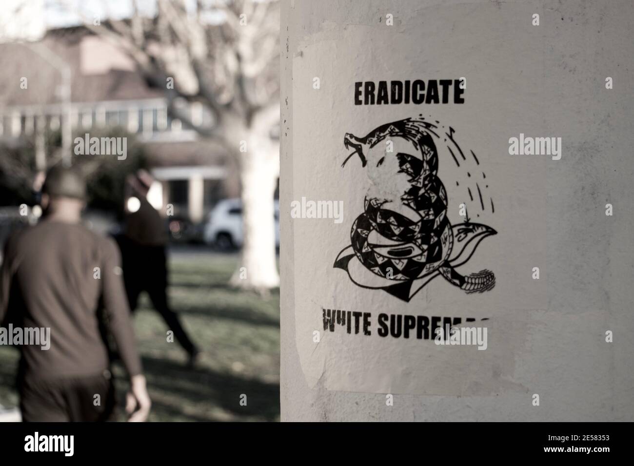'Eradicate White Supremacy' flyer seen at Lake Merritt with the back of black man walking away. Stock Photo
