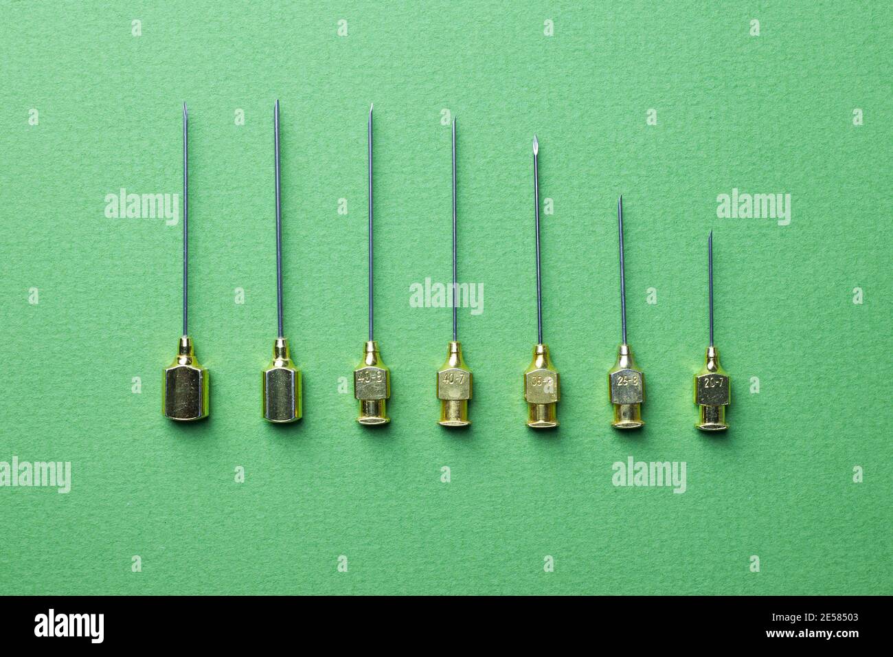 A set of needles for old syringes of different sizes and thicknesses. Green background Stock Photo