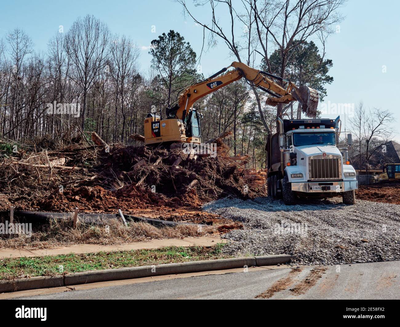 Digger or excavator and dump truck clearing land for new construction building lot in Pike Road Alabama, USA. Stock Photo