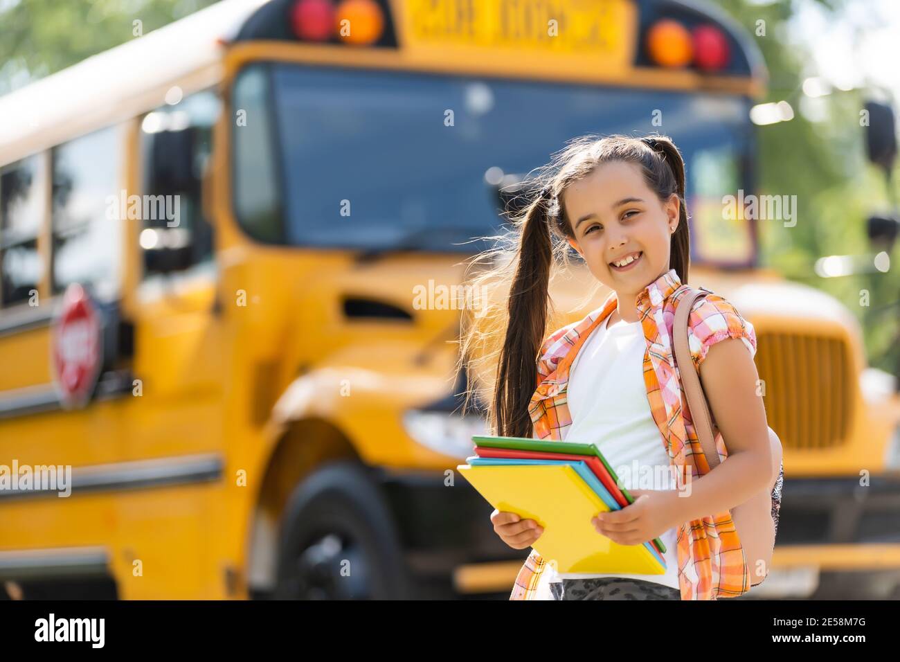 Little girl standing by a big school bus door with her backpack Stock
