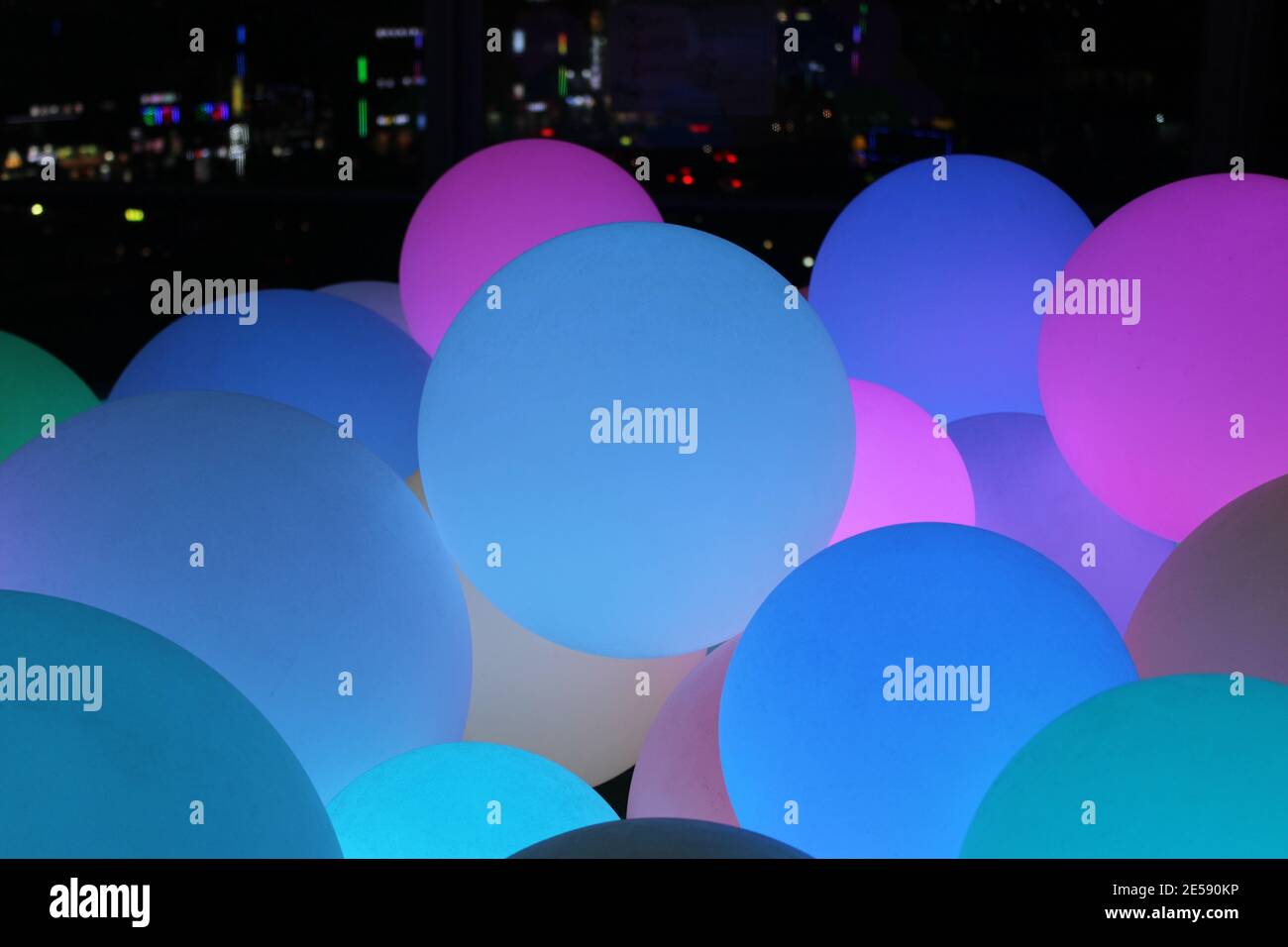 Festive multicolored bubble-like holiday lights against a lit-up skyline Stock Photo