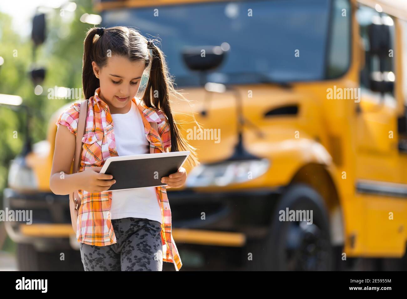 Little girl standing by a big school bus door with her backpack Stock