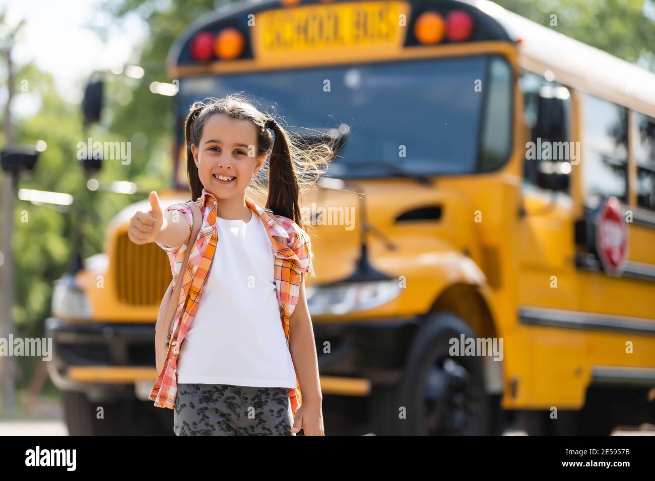 Little girl standing by a big school bus door with her backpack Stock