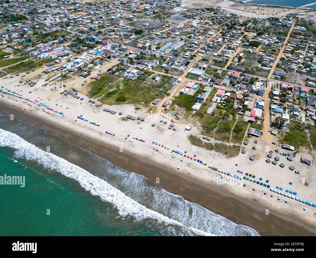 Aerial drone view of the beach, tourists, sea and waves splashing in the coast of the town Playas General Villamil, Ecuador. Sunny day. Stock Photo