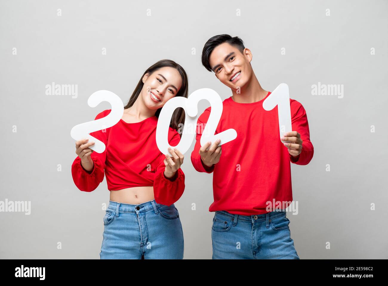 Happy cute Asian couple smiling and showing number 2021 for new year concept on light gray studio background Stock Photo