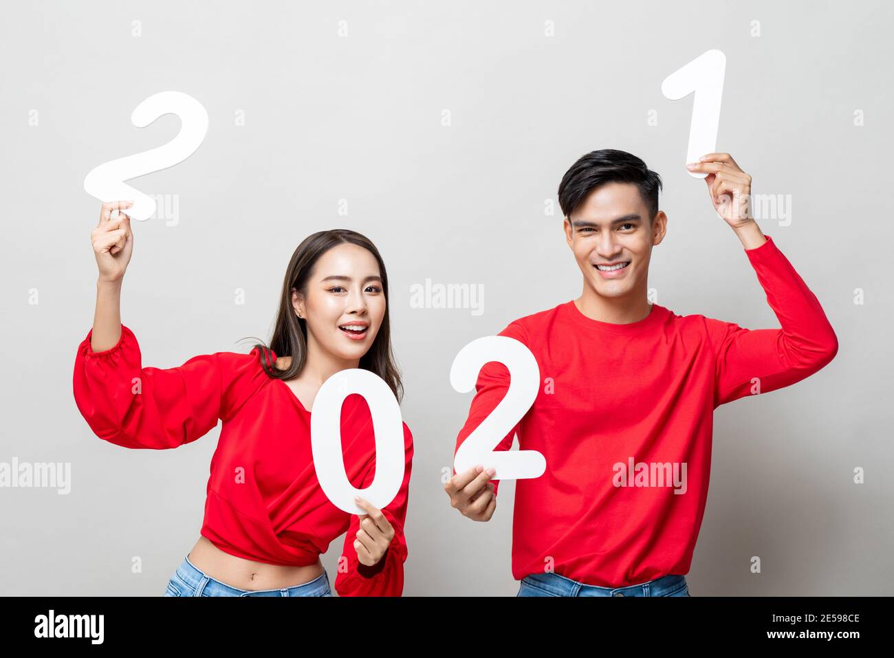 Happy Asian couple smiling and showing number 2021 for new year concept on isolated light gray studio background Stock Photo