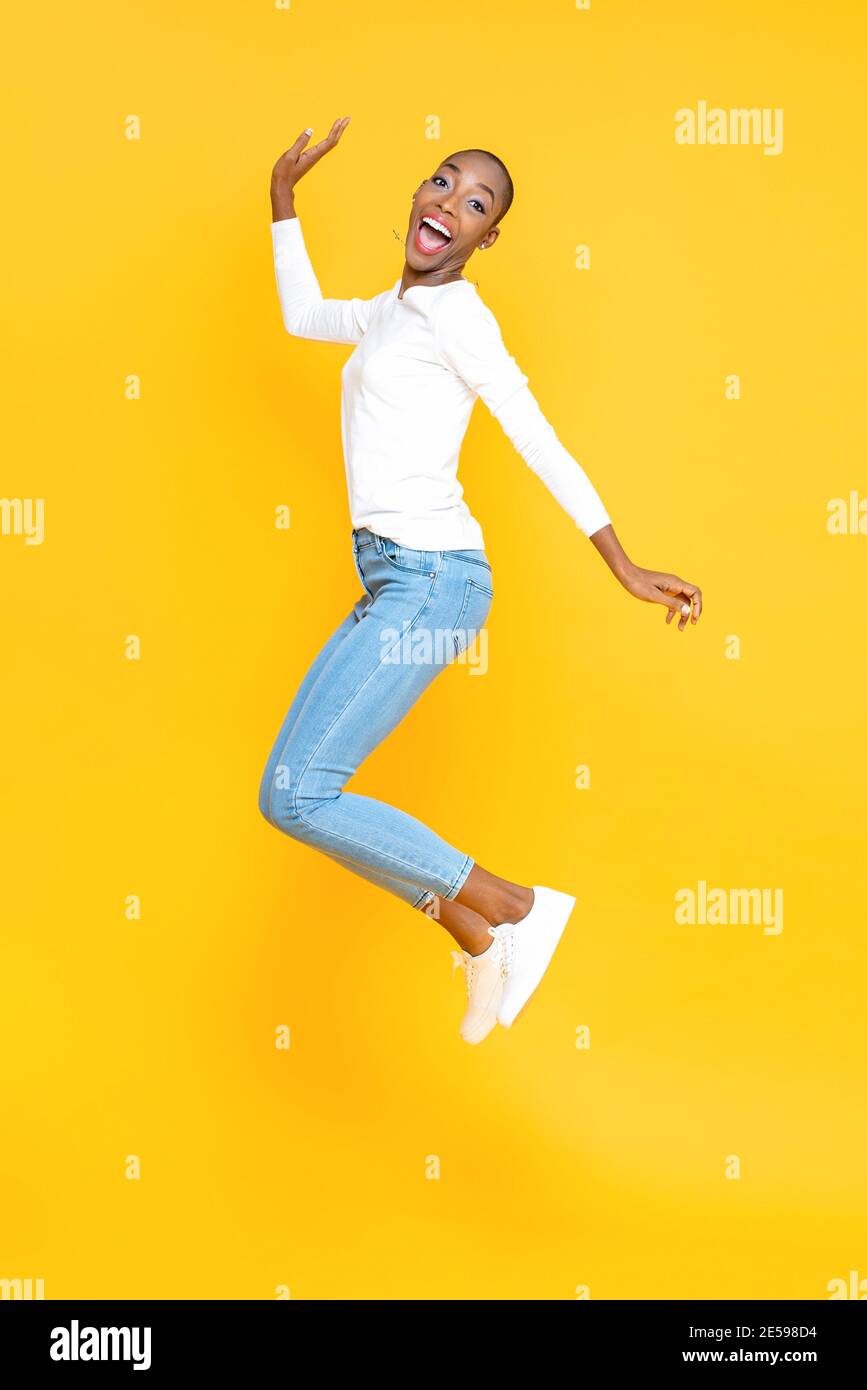 Happy smiling African American woman jumping in yellow isolated studio ...