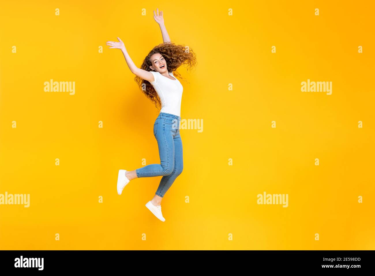 Pretty Woman Jumping Freely With Both Hands Up Isolated In Yellow Color 