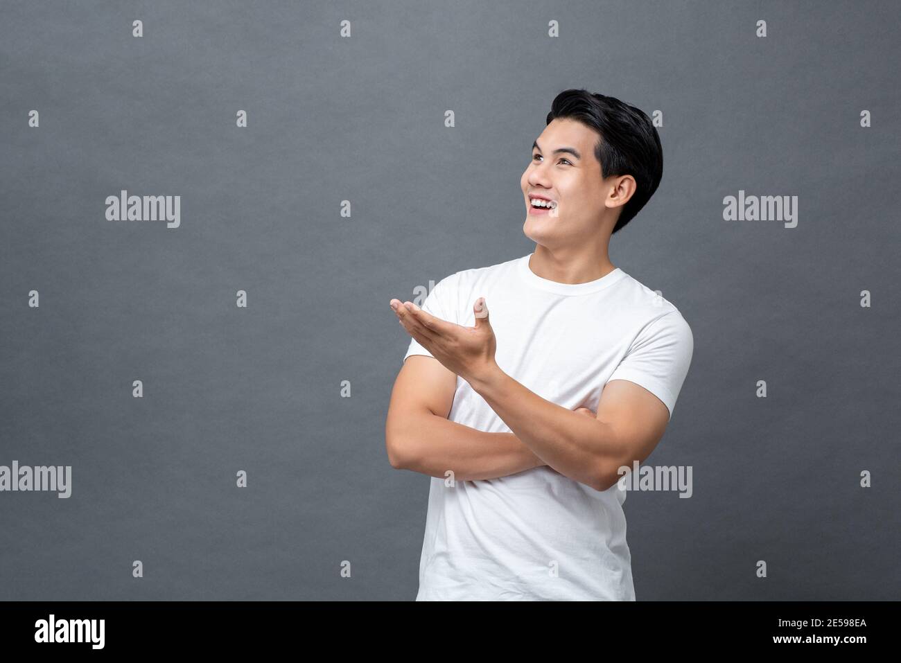 Portrait of smiling young Asian man looking upward and doing open palm gesture isolated on studio gray background Stock Photo