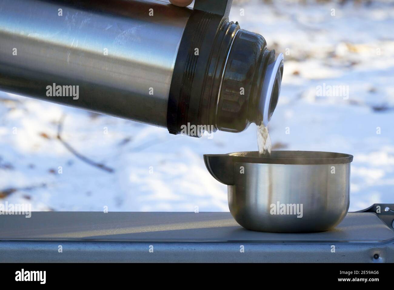 Small thermos with steaming hot drink on snow Stock Photo by