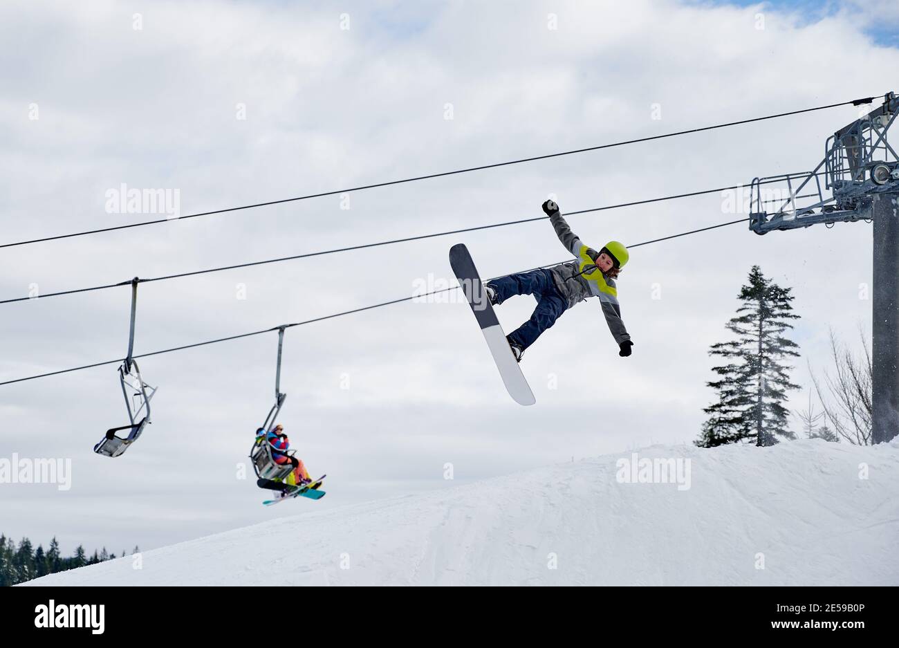Snowboarder doing tricks in the mountains during winter season, flying up high with snowboard against chairlift and sky. Concept of extreme kinds of sport. Low angle view Stock Photo