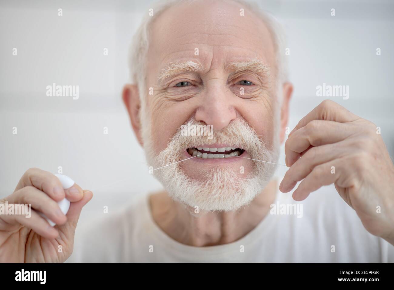 Gray-haired man in white tshirt cleaning teeth with a floss Stock Photo