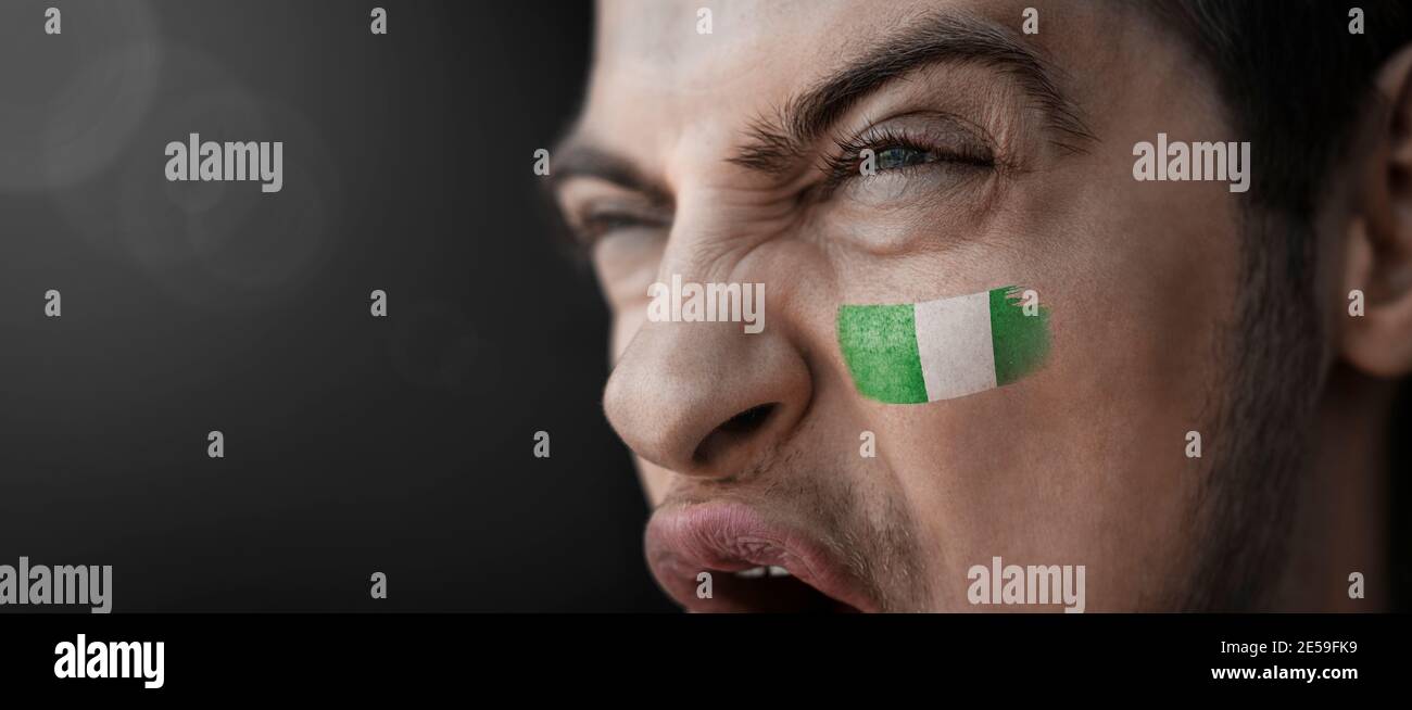 A screaming man with the image of the Nigeria national flag on his face Stock Photo