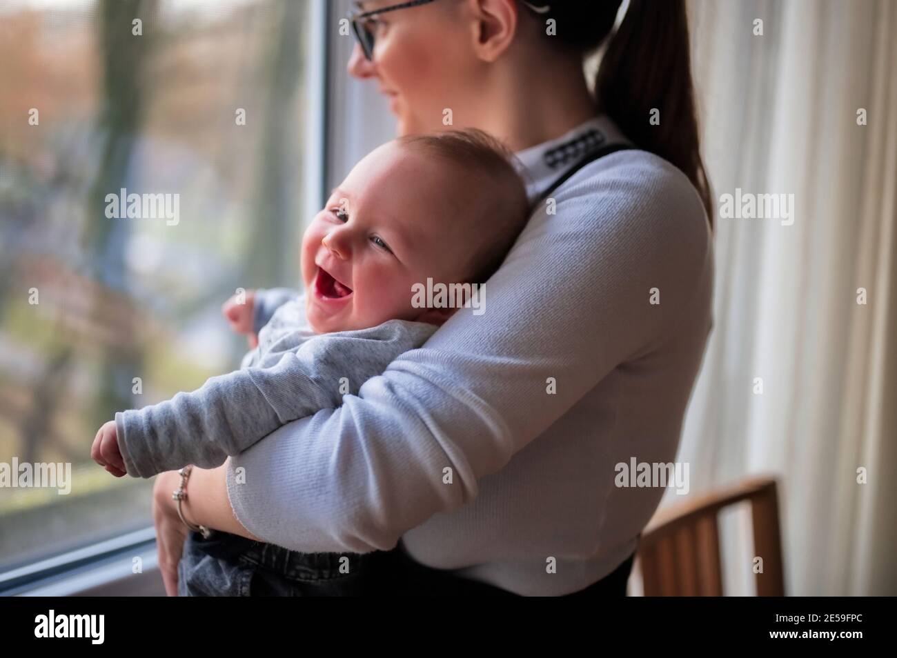 Mother standing by the window and holding cute little baby Stock Photo