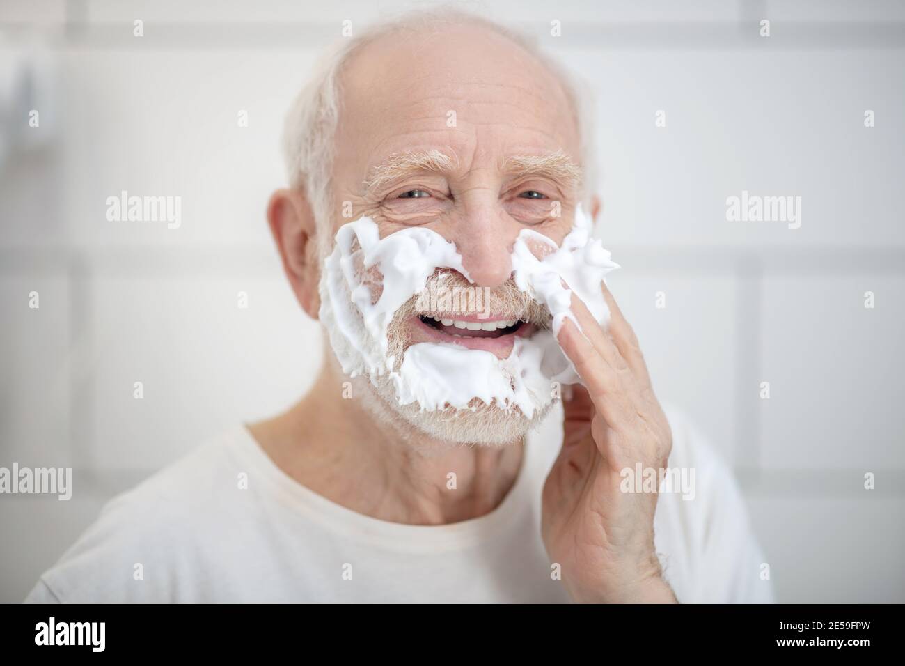 Gray-haired man in white tshirt shaving in the bathroom Stock Photo