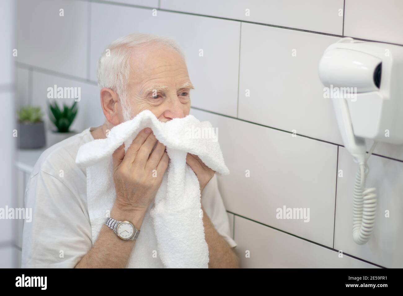 Gray-haired man in white tshirt wiping his face with the towel Stock Photo