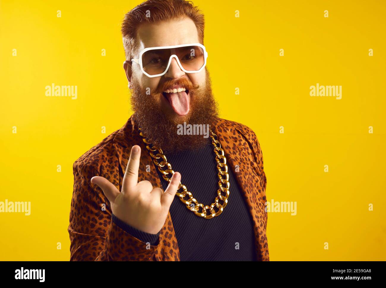 Funny eccentric bearded man in extravagant outfit doing horn sign and sticking tongue out Stock Photo
