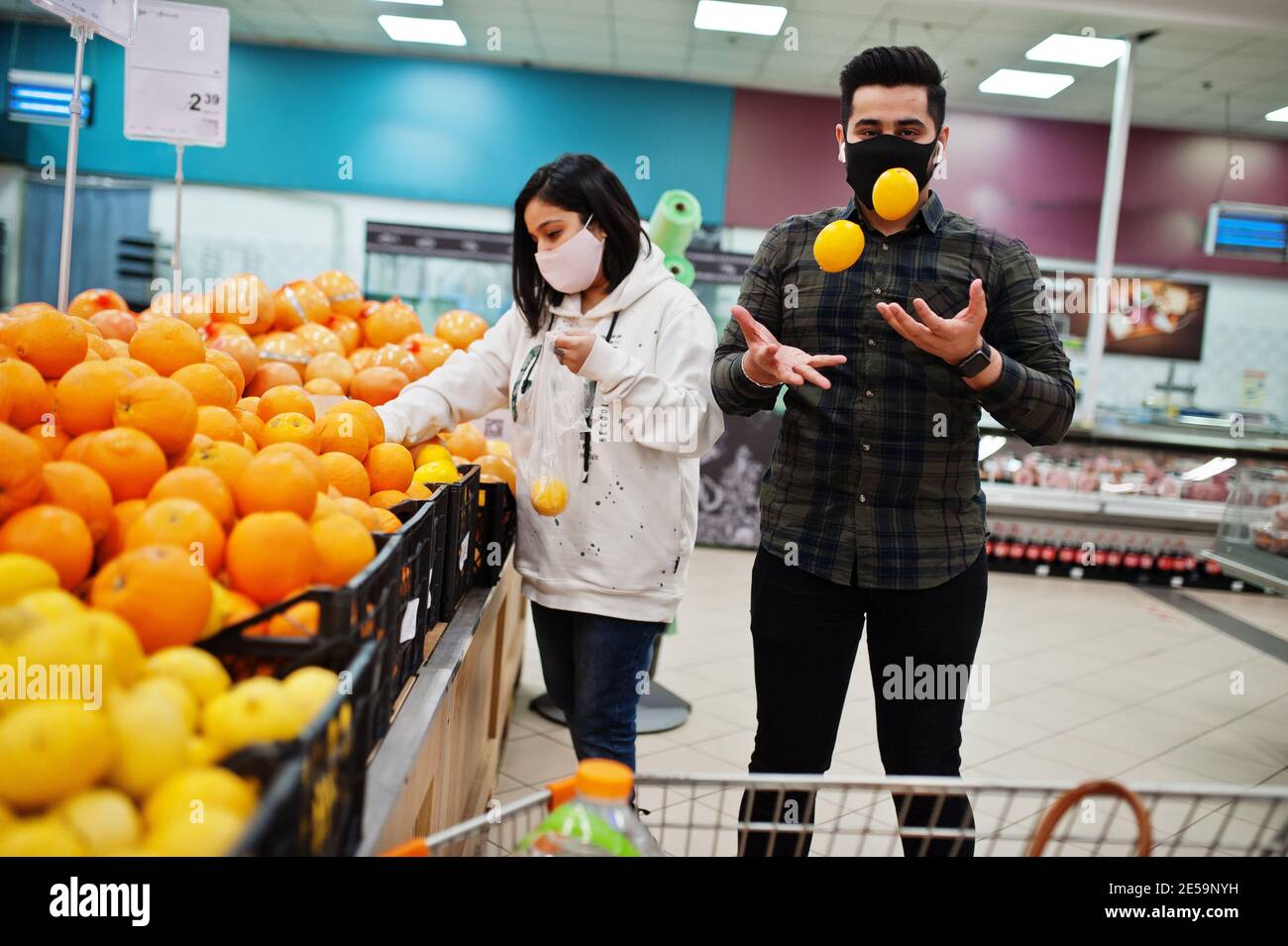 Asian couple wear in protective face mask shopping together in supermarket during pandemic. Choosing different fruits. Stock Photo