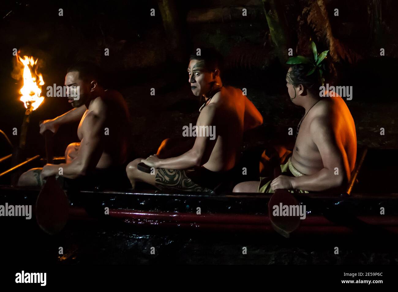 Three fierce tattooed Maori warriors paddling an ancient waka (warrior canoe) down the Wai-o-whiro stream at night ,Mitai Maori Village, New Zealand Stock Photo