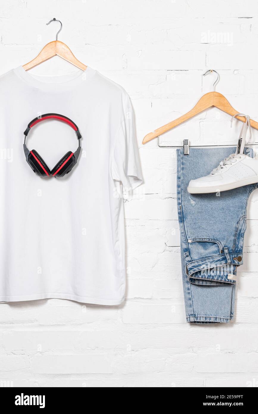 blue jeans, white t-shirt, sneaker and wireless headphones on hangers near brick wall Stock Photo