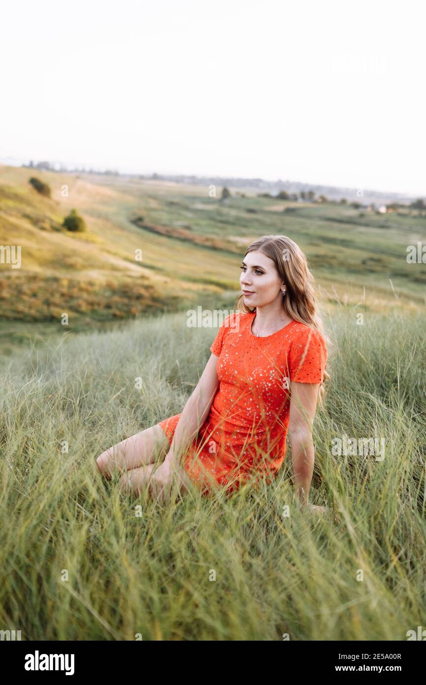 Portrait of a beautiful woman is sitting in green grass on field ...