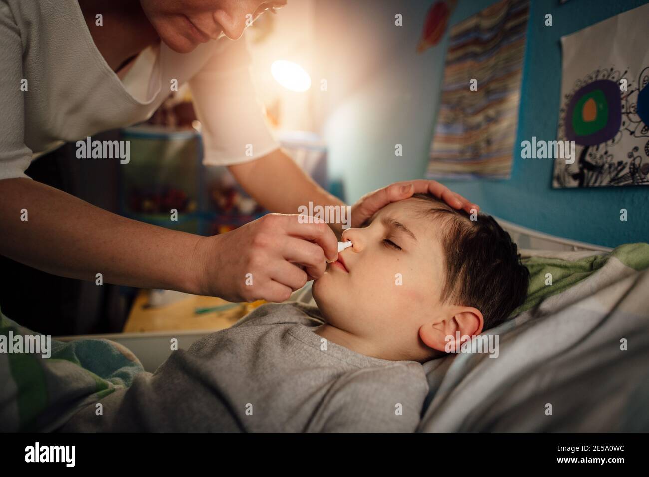 A sick child lying in bed with a stuffy nose. A mother clearing a blocked nose of her son in his bedroom at night. Stock Photo
