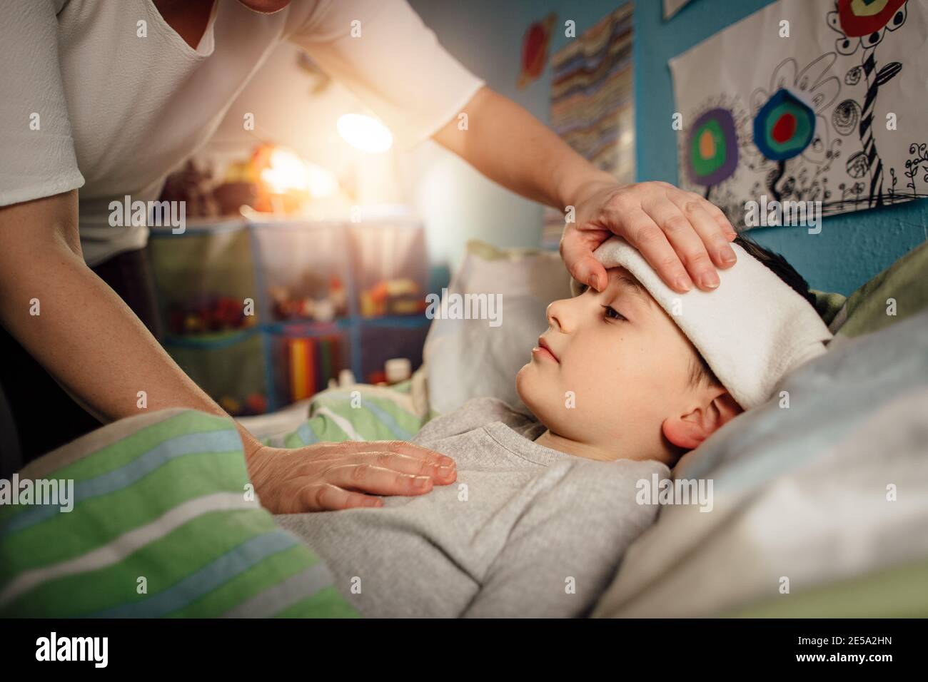 A sick child lying in a bed with a wet cloth on his forehead. A mother taking care of her ill child at home in the night. Stock Photo