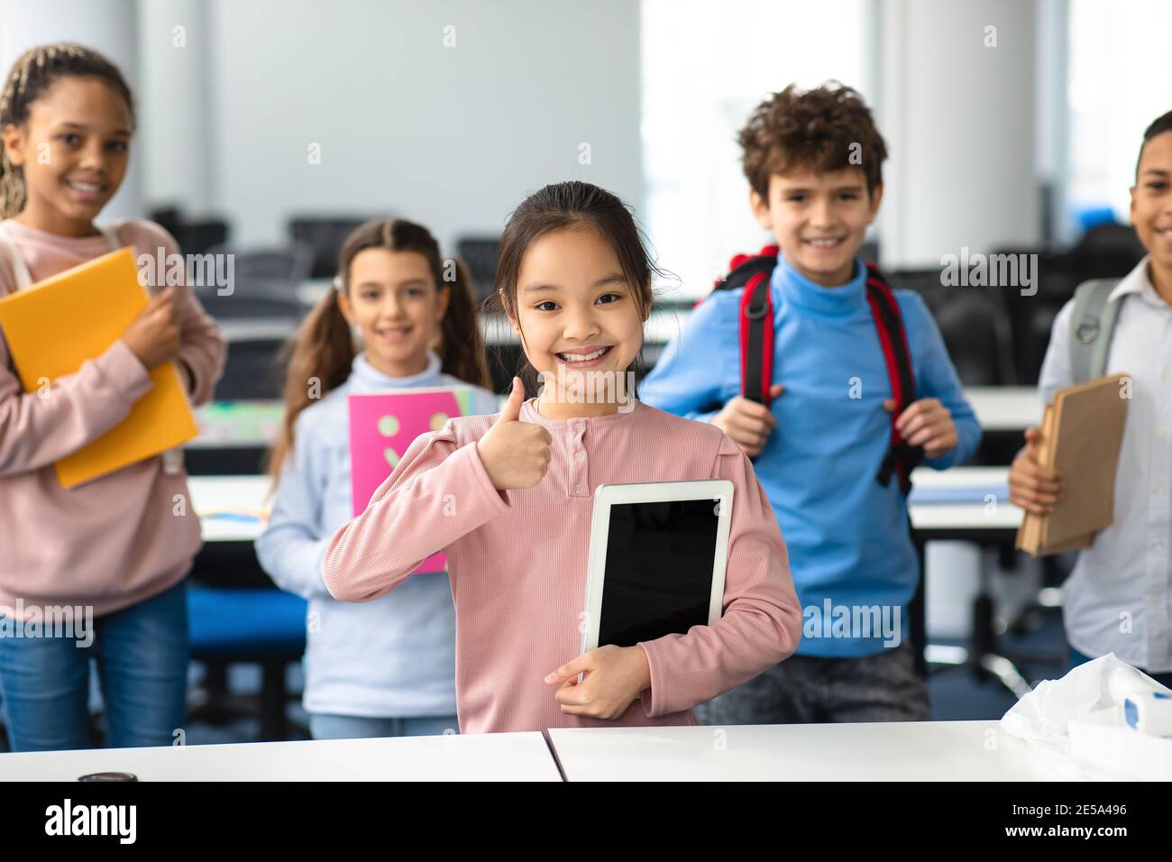 Smiling asian girl holding tablet showing thumbs up gesture Stock Photo