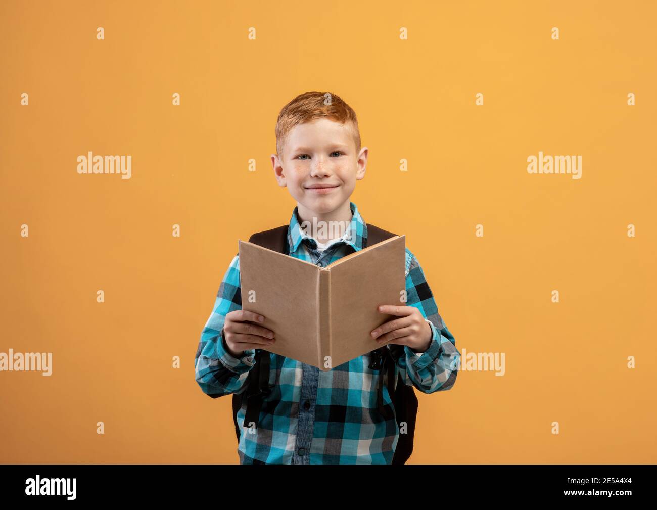 Cute ginger kid schooler reading book, yellow studio background Stock
