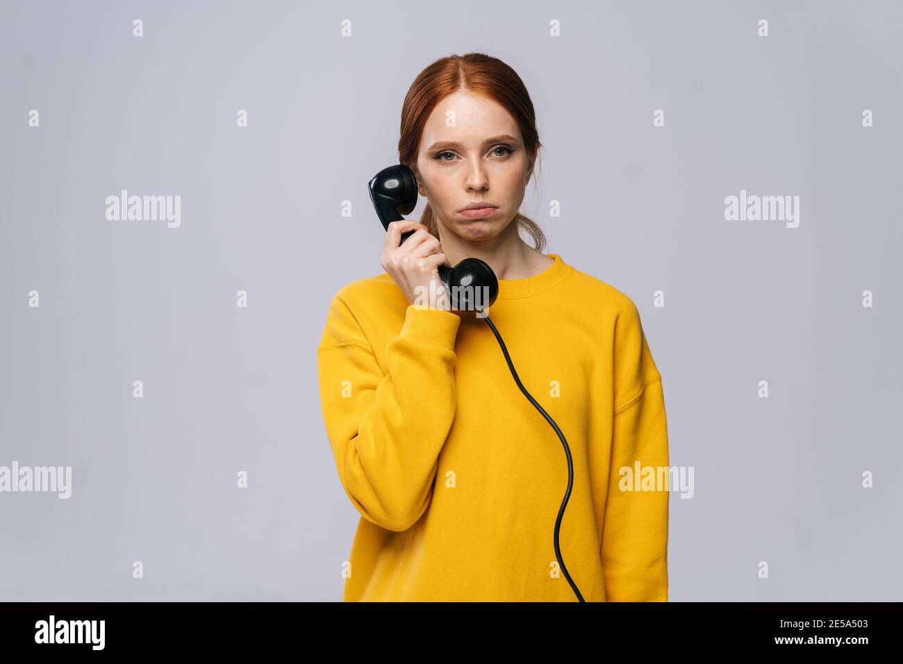 Sad unhappy young woman in stylish yellow sweater talking on retro phone and looking at camera Stock Photo
