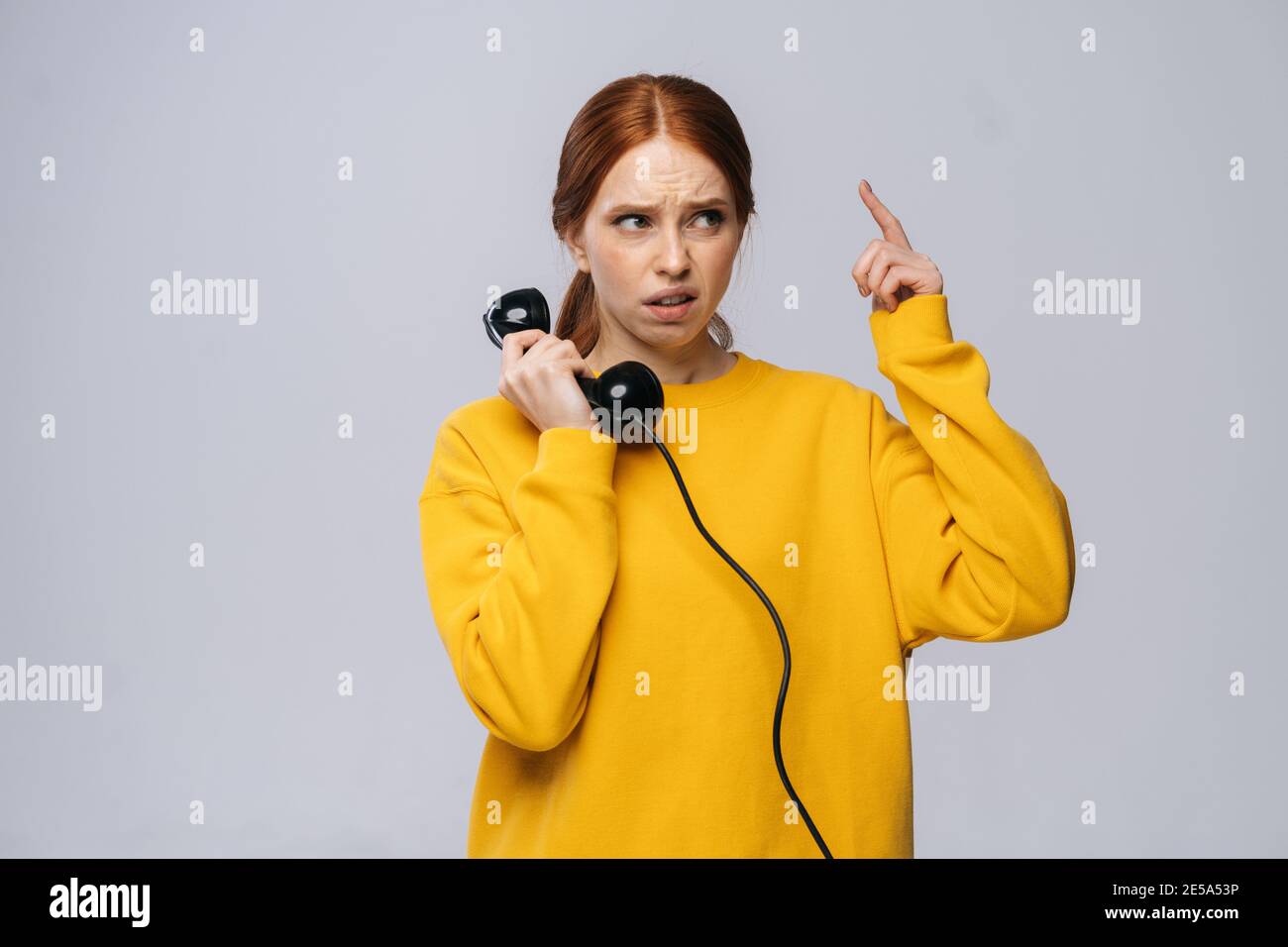Confused young woman in stylish yellow sweater talking on retro phone and looking away Stock Photo