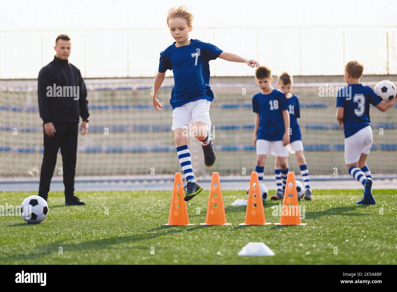 Kids on sports soccer training. Boys running balls and jumping over cones. Agility exercises for youths in football team. Coach of football team coach Stock Photo