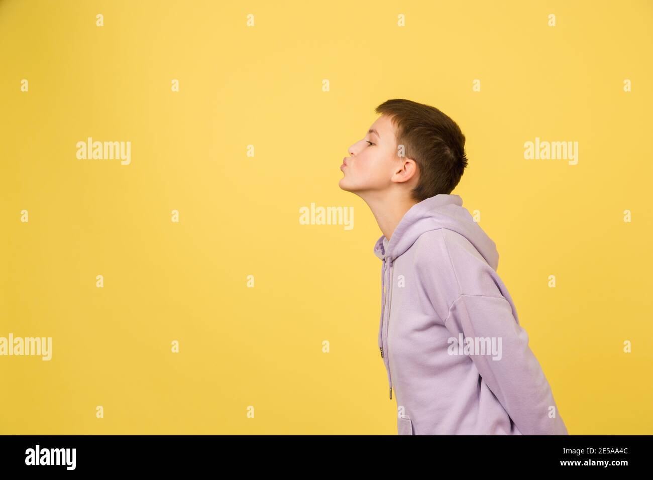 Kissing, sending kisses. Caucasian girl's portrait isolated on yellow background with copyspace. Beautiful female model in hoodie. Concept of human emotions, facial expression, sales, ad, fashion. Stock Photo