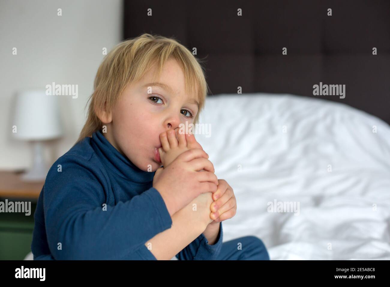 Cute blond toddler child, sucking his foot thumb, making funny faces, laughing Stock Photo