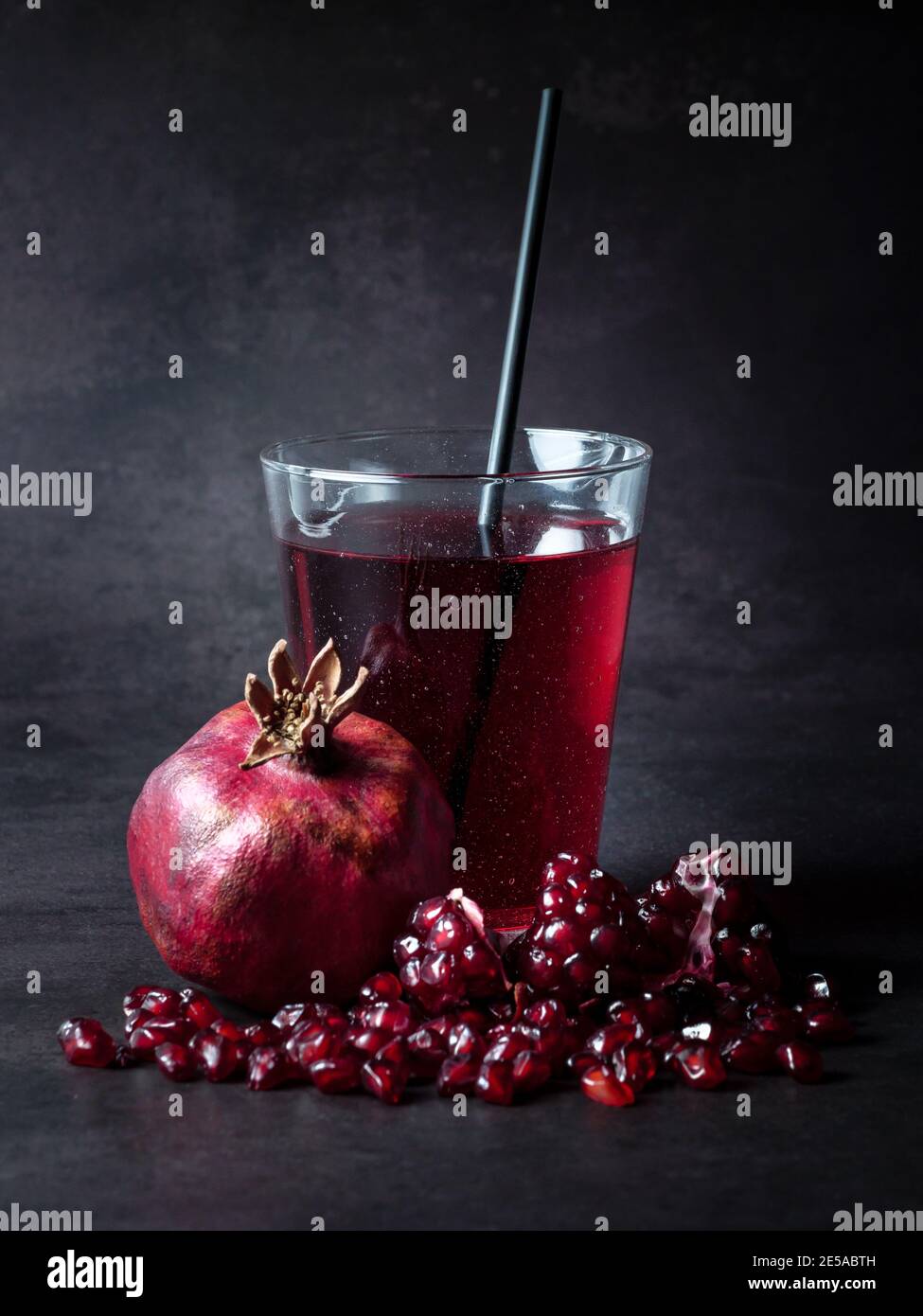 Pomegranate juice in a glass with cocktaile straw and fresh grenadine fruit on the table at black background. Popular fruit in Azerbaijan and Turkey. Stock Photo