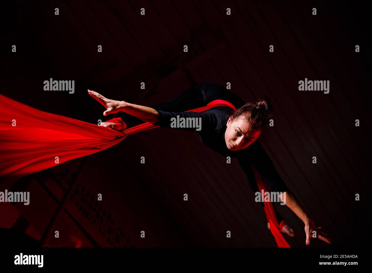 A sports girl performs gymnastic and circus exercises on red silk. Studio shooting on a dark background. Aerial gymnastics on canvas Stock Photo