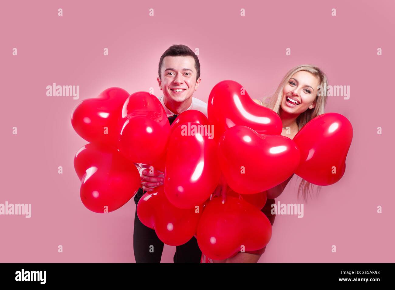 Valentines day. Happy young couple with heart shaped balloons on pink ...