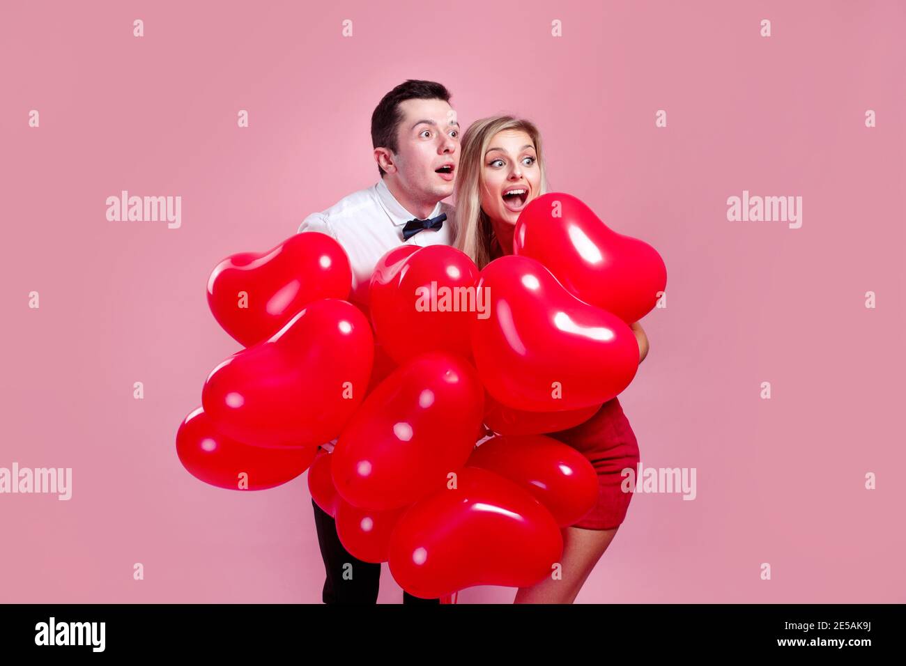Valentines day. Surprised young couple with balloons heart on pink ...